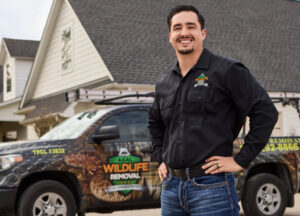 A good looking wildlife technician standing in front of a wildlife removal truck at a customer's home